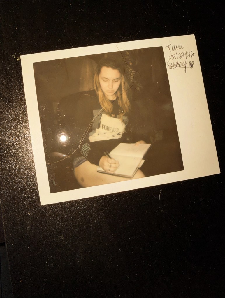 Warm-toned photo of a polaroid showing Tara journaling